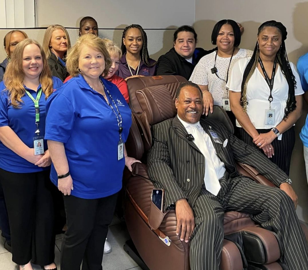 Robert Nelson seated in a Luraco medical massage chair surrounded by 911 dispatch and public safety staff